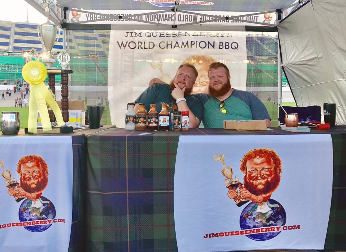 Jim Quessenberry and Arthur McDaniel in front of a table filled with BBQ equipment.